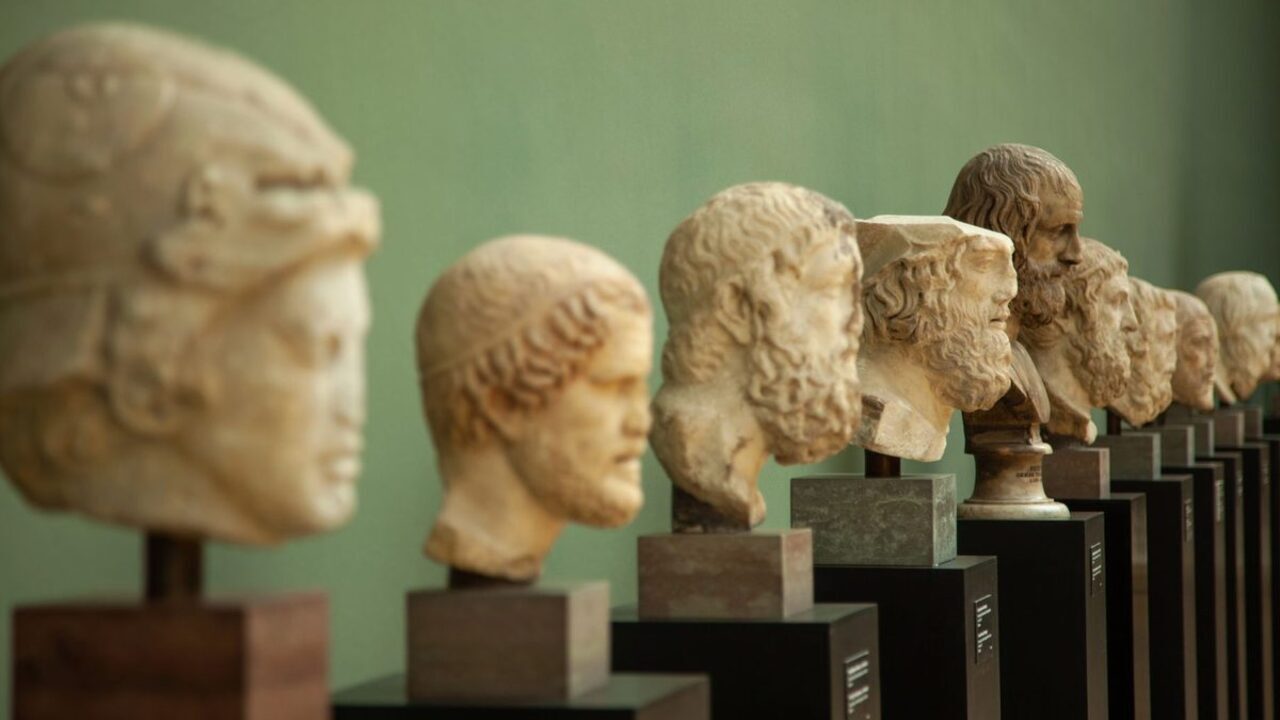 Mai multe busturi și capete sculptate în piatră sunt expuse pe socluri într-o galerie de artă.
