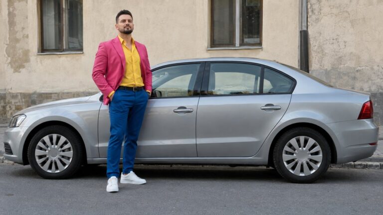 Bărbat adult îmbrăcat ostentativ lângă o mașină fără emblemă.