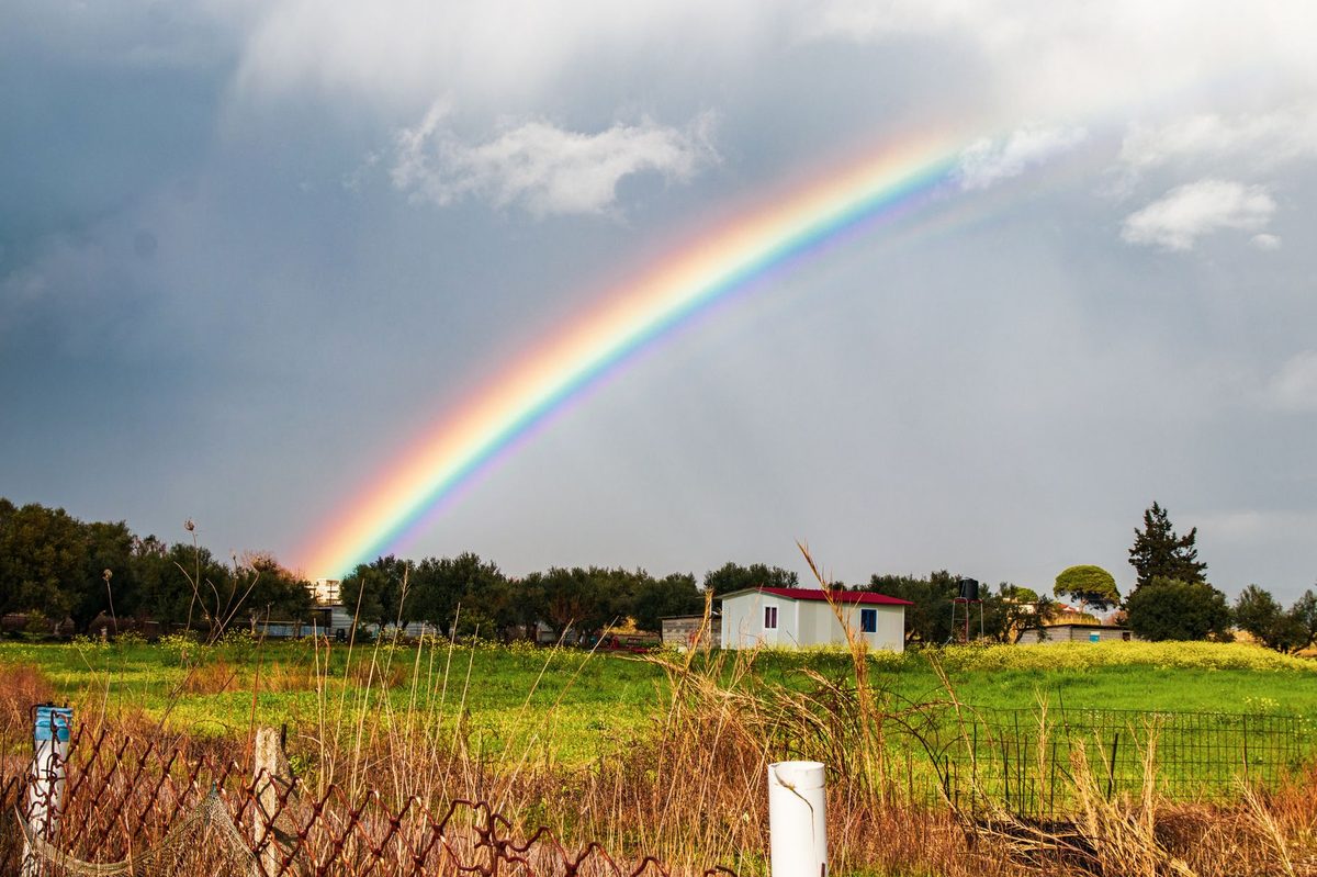 Curcubeu luminos apărut deasupra unui peisaj natural după ploaie