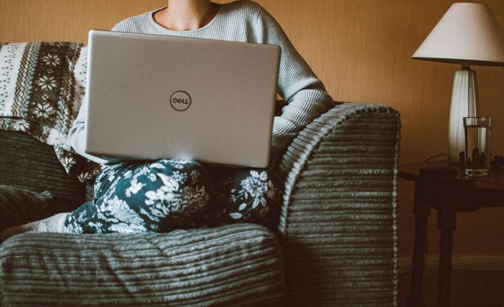 Persoană cu un laptop în poală, așezată într-un fotoliu