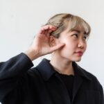 Femeie cu mâna la ureche ascultând atent, simbol al percepției auditive și superstiției