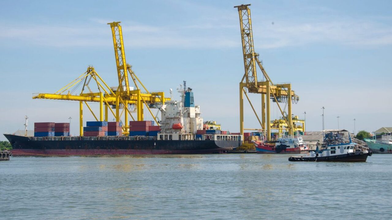O navă de transport maritim acostează într-un port comercial lângă macarale galbene.