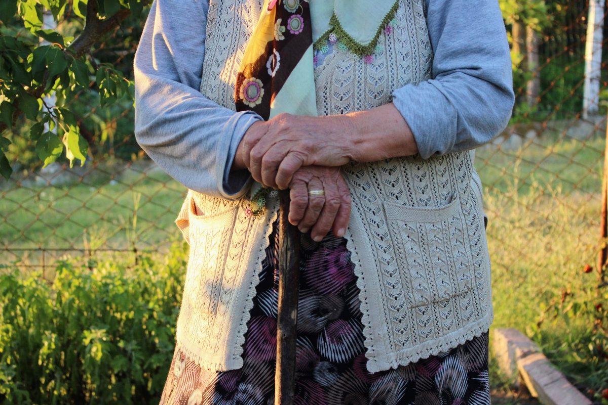 Mâini de bunică în vârstă împletite într-un cadru tradițional rural