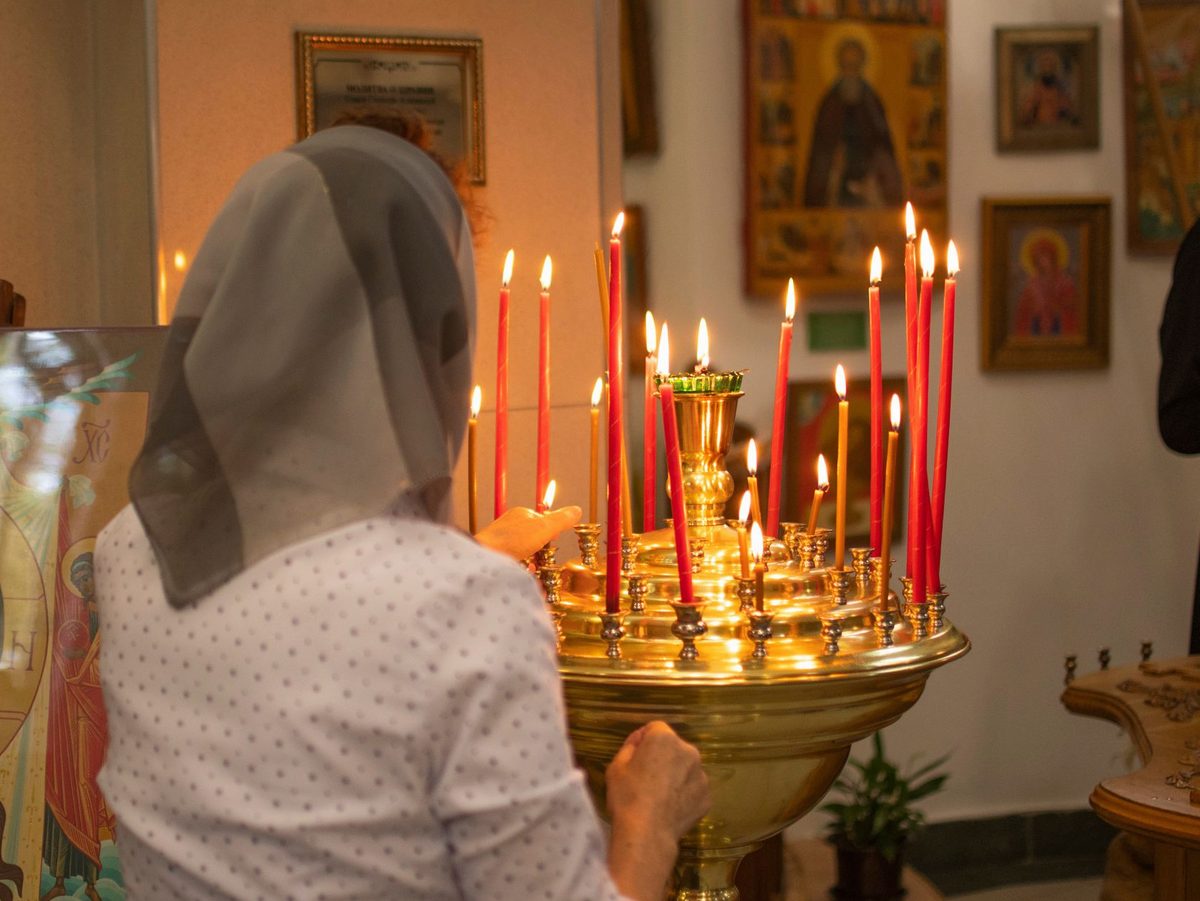 Femeie rugându-se cu evlavie lângă lumânări aprinse în biserică