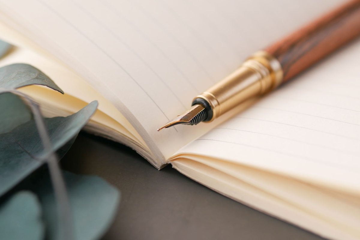 Stilou scriind note pe paginile unui caiet din hârtie