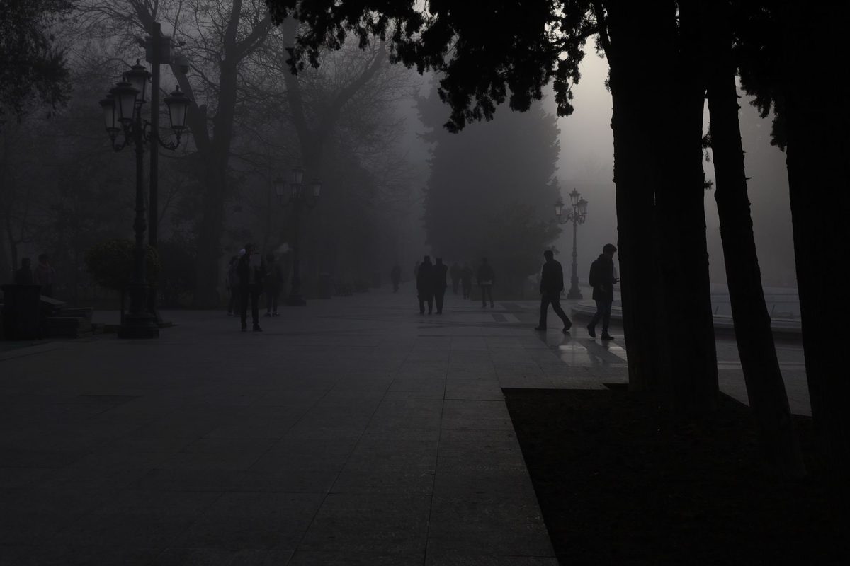 Silueta unui bărbat mergând pe o alee din parc învăluită în ceață