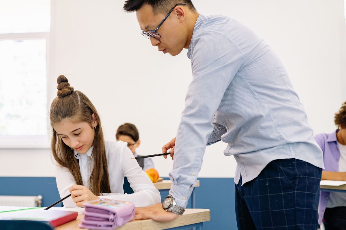 Cadru didactic care ajută un elev la o masă de studiu din școală.
