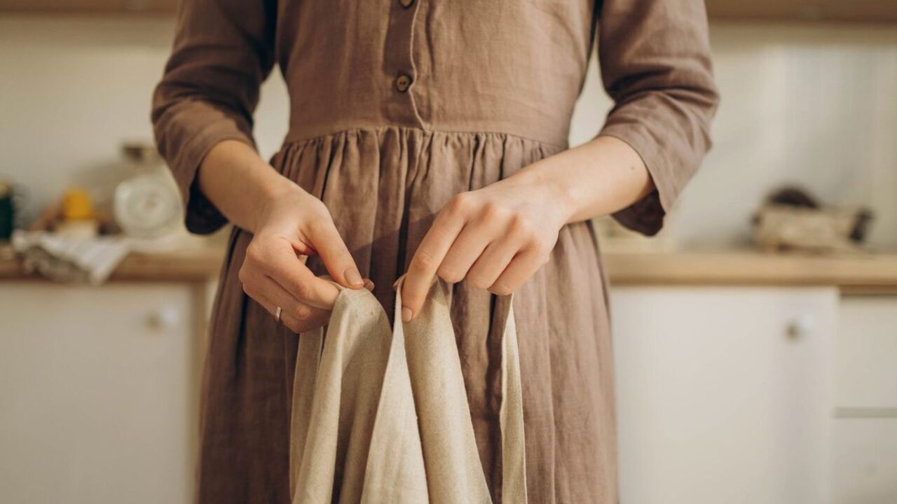 O persoană atinge cu ambele mâini pliurile fine ale unei rochii din material textil natural.