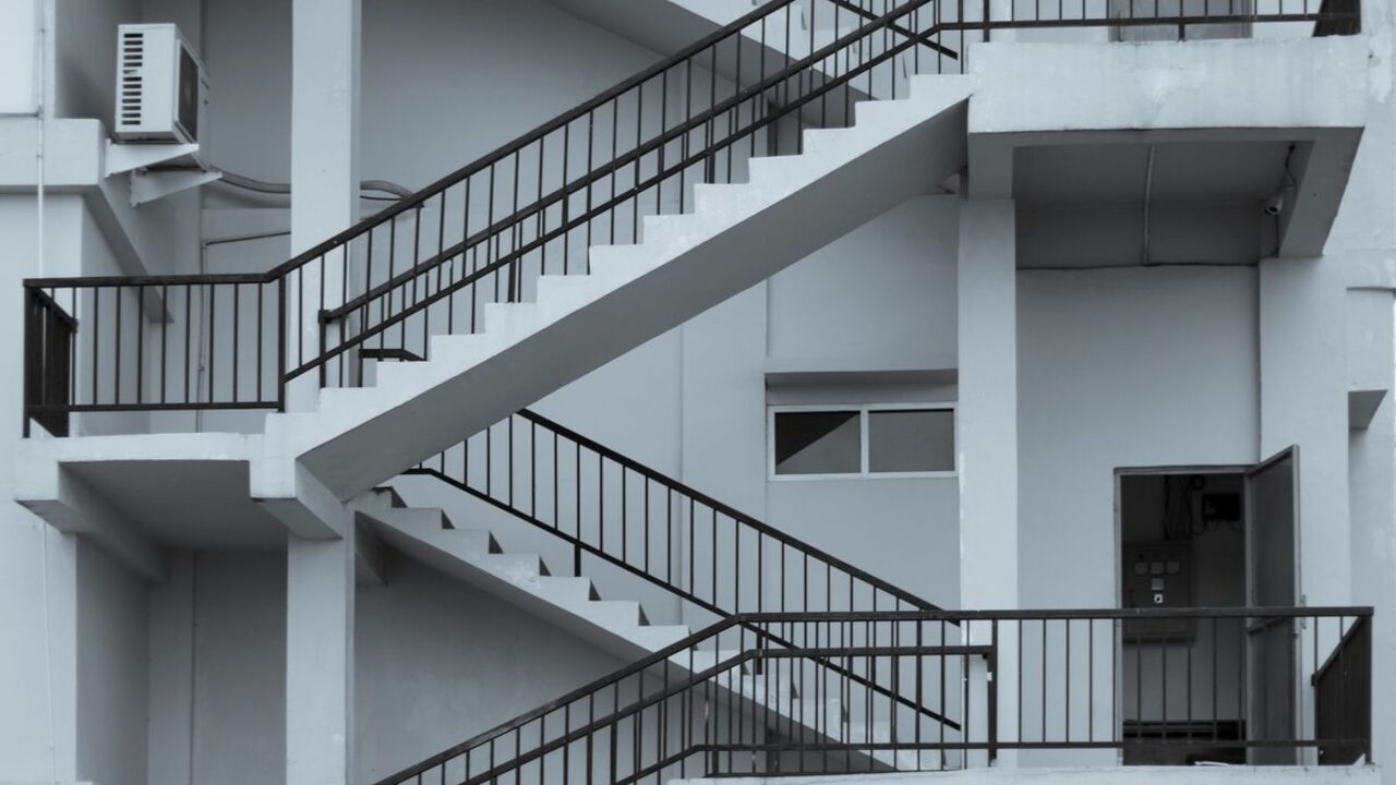O casă a scării dintr-un bloc modern cu trepte albe și balustrade metalice negre înclinate.