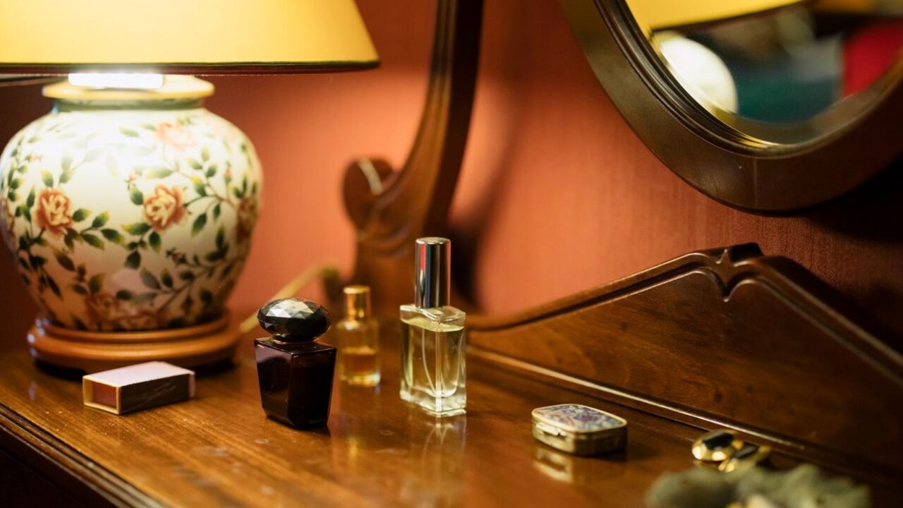 Sticluțe elegante de parfum sunt așezate pe o masă de toaletă din lemn cu oglindă.