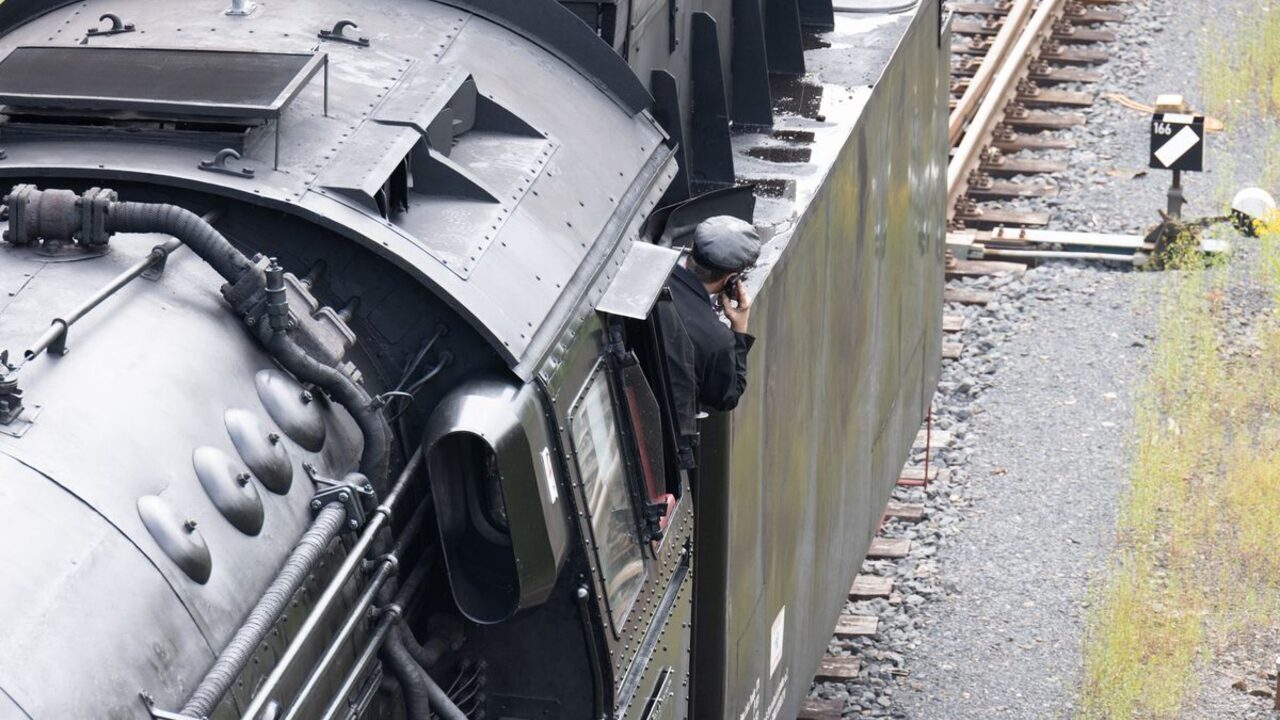 Un mecanic de locomotivă privește atent înainte de la fereastra cabinei de tren.