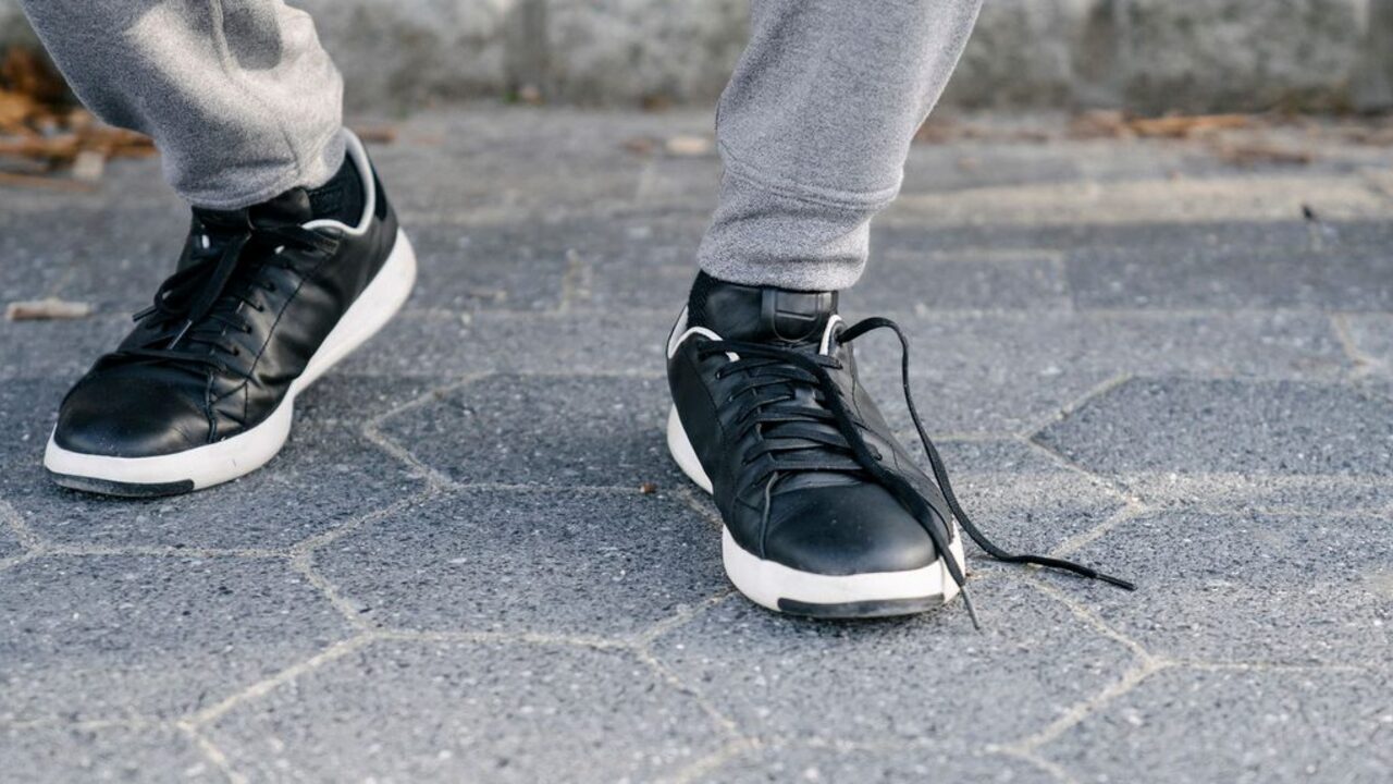 Pantoful sport negru al unei persoane care merge pe stradă are șireturile desfăcute pe pavaj.
