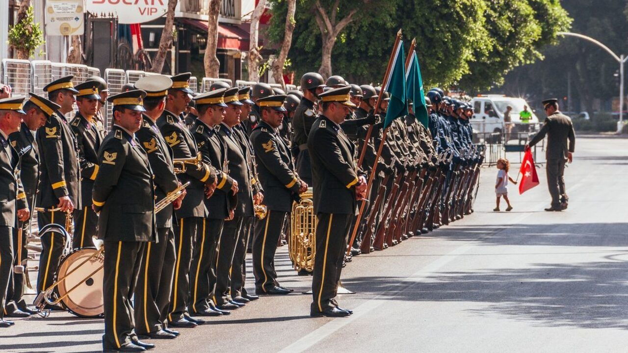 Soldați în uniforme ceremoniale stau aliniați în formație pe marginea unui bulevard.