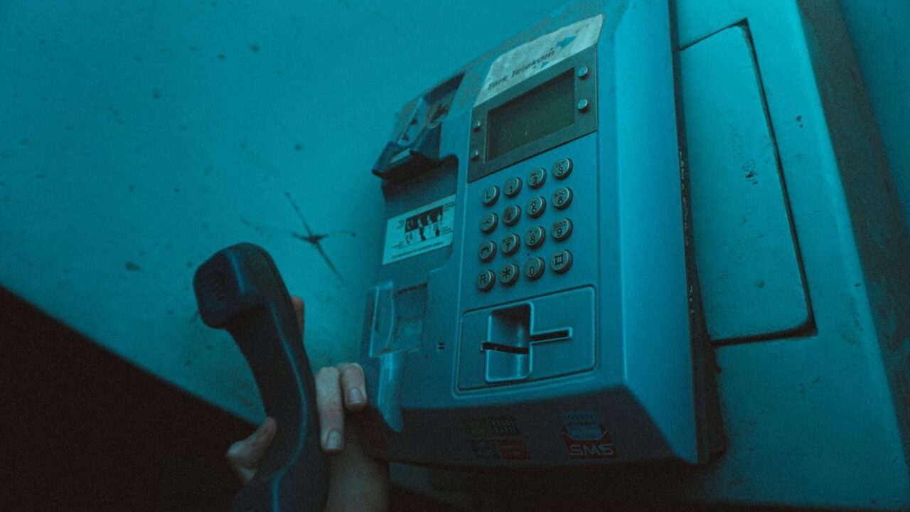 Receptorul unui telefon public din metal este desprins din furcă într-o lumină albastră.